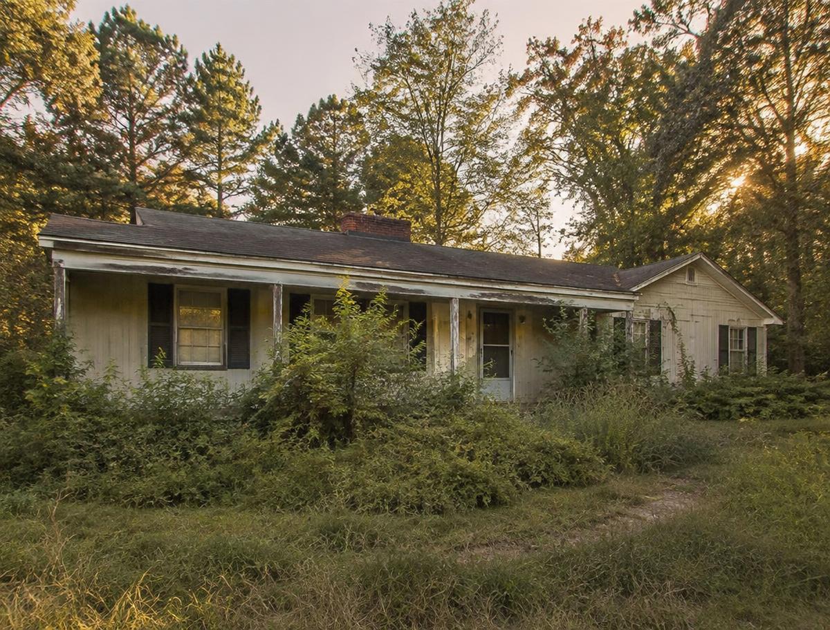 An older one-storey house with faded paint and an overgrown yard in soft evening light